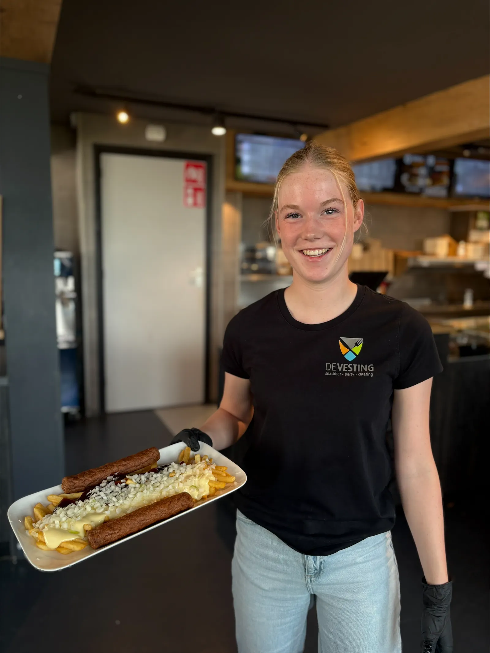 Medewerker van De Vesting met een schaal frites met frikandel in de zaak